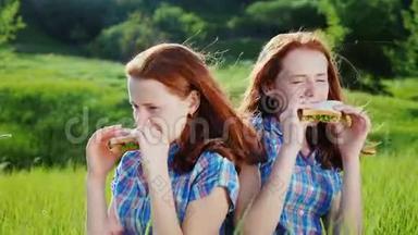 两对十几岁女孩的双胞胎吃三明治。 在绿色草地上风景如画的地方。 在清澈的春天举行家庭野餐